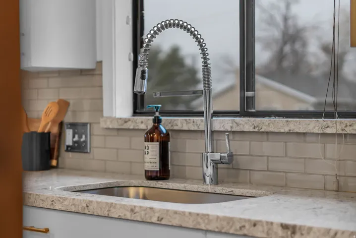 Kitchen view of backsplash, light stone counters, and white cabinetry