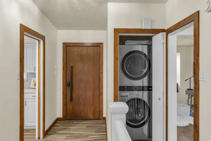 Laundry area with stacked washer and clothes dryer, a textured ceiling, and light wood-type flooring