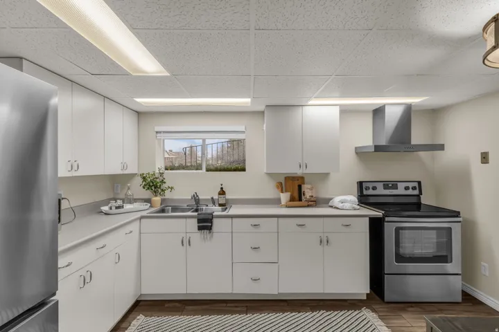 Kitchen with stainless steel appliances, light countertops, white cabinets, dark wood-type flooring, and a drop ceiling