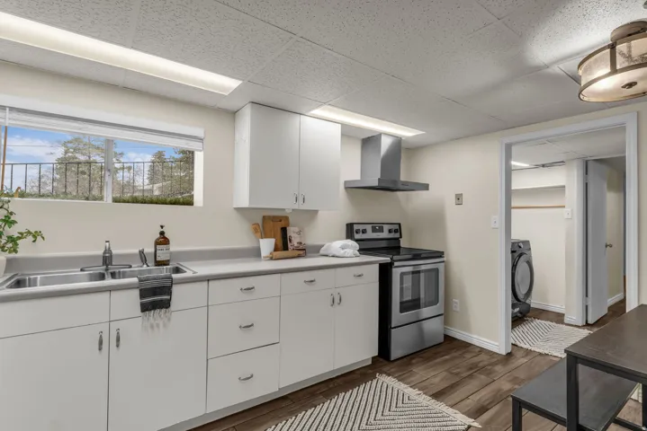 Kitchen with stainless steel electric stove, white cabinets, light countertops, dark wood-type flooring, and a paneled ceiling