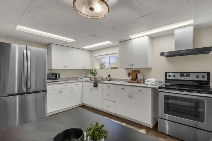 Kitchen with stainless steel appliances, light countertops, ventilation hood, white cabinets, and a paneled ceiling