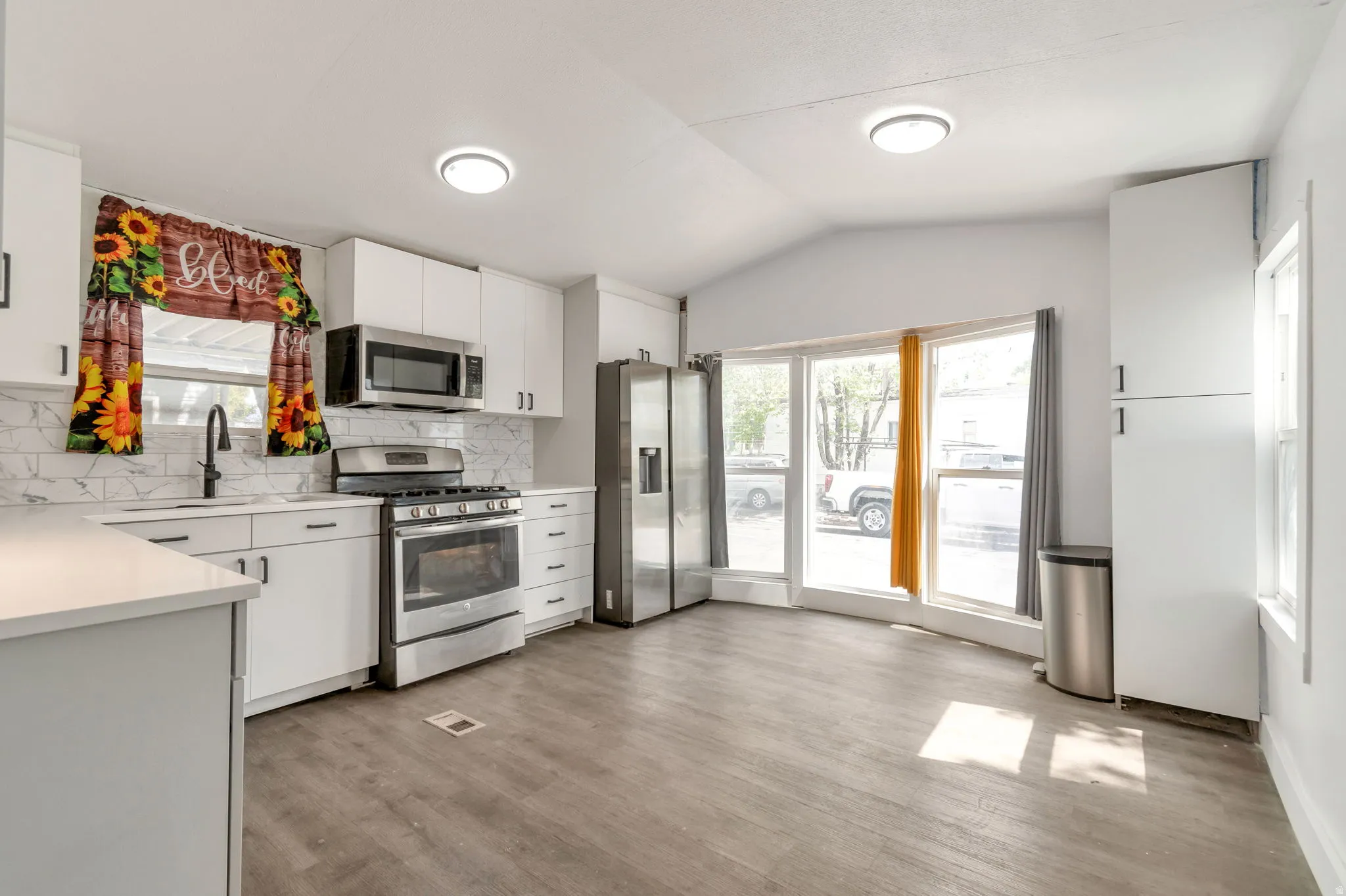 Kitchen with stainless steel appliances, white cabinets, backsplash, light wood finished floors, and vaulted ceiling