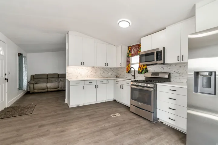 Kitchen featuring stainless steel appliances, tasteful backsplash, white cabinets, dark wood-type flooring, and vaulted ceiling