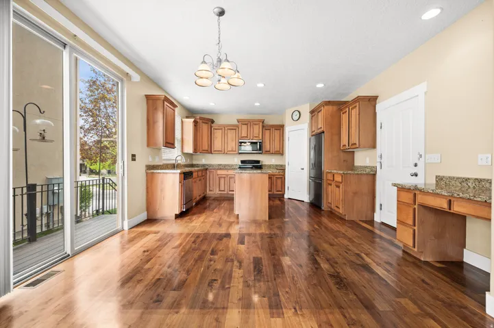 Kitchen with wood finish cabinets, light stone counters, hanging lights, and dark wood finished floors