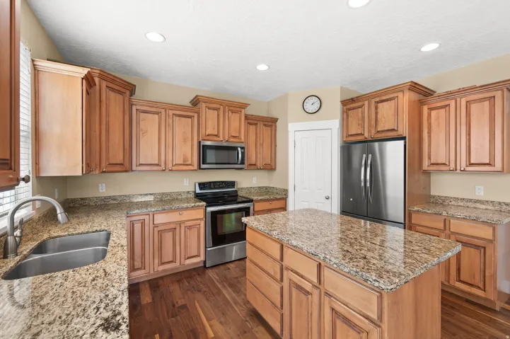 Kitchen featuring stainless steel appliances, light stone countertops, a center island, dark wood-style flooring, and wood finish cabinets
