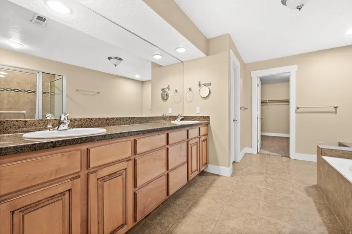 Full bath featuring double vanity, a walk in closet, a garden tub, a stall shower, and light tile patterned floors