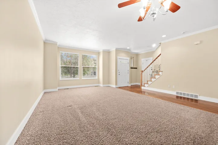 Unfurnished living room featuring a ceiling fan, carpet, ornamental molding, and a textured ceiling