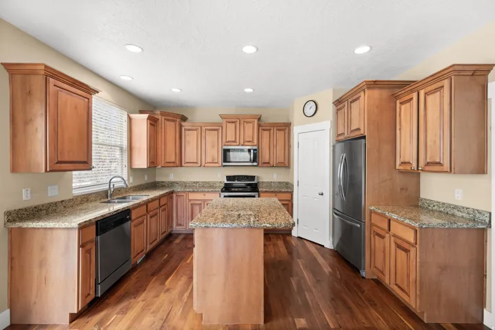 Kitchen featuring light stone countertops, a center island, stainless steel appliances, wood finish cabinetry, and dark wood-style floors