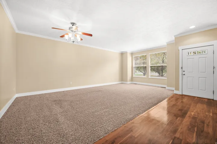 Unfurnished living room featuring ornamental molding, ceiling fan, wood finished floors, and carpet floors