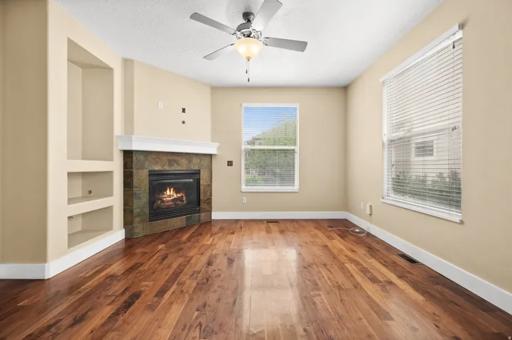 Unfurnished living room with a ceiling fan, dark wood-style flooring, a tile fireplace, built in features, and a textured ceiling