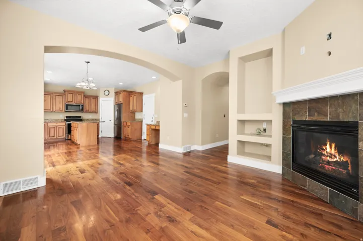 Unfurnished living room featuring built in shelves, arched walkways, a tiled fireplace, ceiling fan, and a chandelier