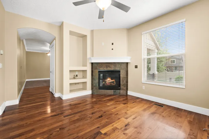 Unfurnished living room with built in shelves, ceiling fan, arched walkways, dark wood-style flooring, and a textured ceiling
