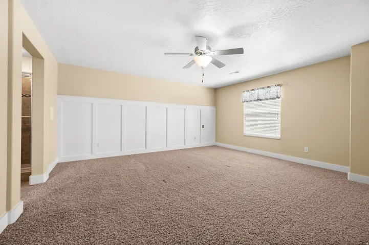 Spare room with a decorative wall, carpet flooring, ceiling fan, a textured ceiling, and wainscoting