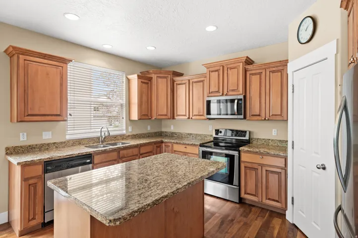 Kitchen featuring stainless steel appliances, wood finish cabinetry, dark wood-style flooring, light stone counters, and recessed lighting