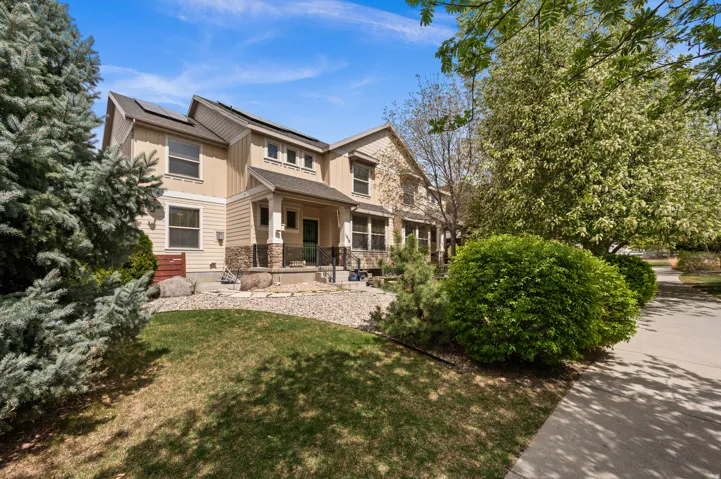 Rear view of house featuring a lawn, roof mounted solar panels, stone siding, and covered porch