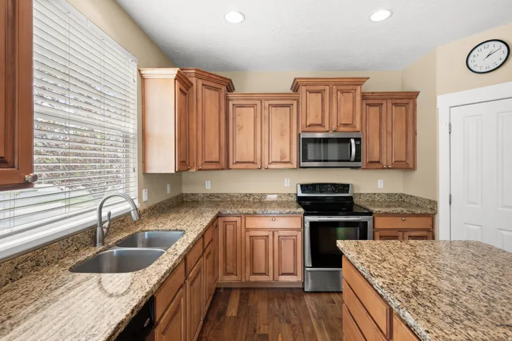 Kitchen featuring stainless steel appliances, light stone countertops, wood finish cabinetry, and recessed lighting