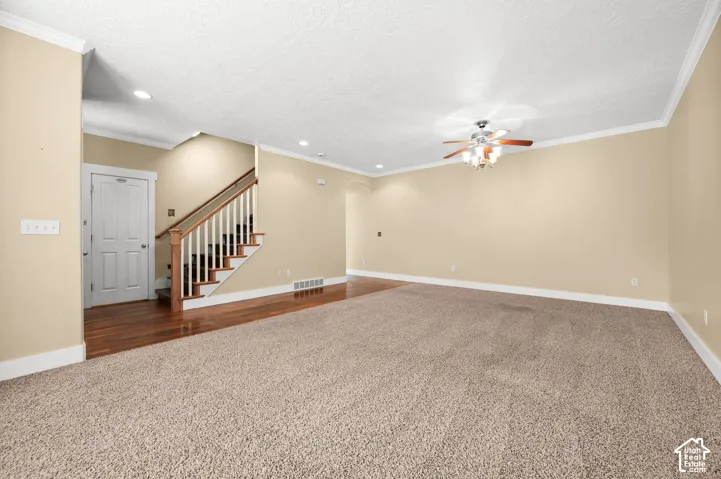 Spacious room featuring neutral wall tones, textured carpet flooring, wood-finish stair treads with white balusters, recessed lighting, and a ceiling fan with integrated light fixture