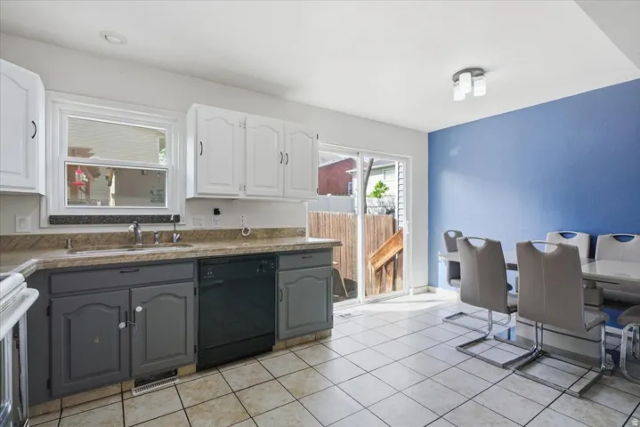 Dual tone kitchen with two tone cabinetry, dishwasher, range, light tile patterned flooring, and dark countertops