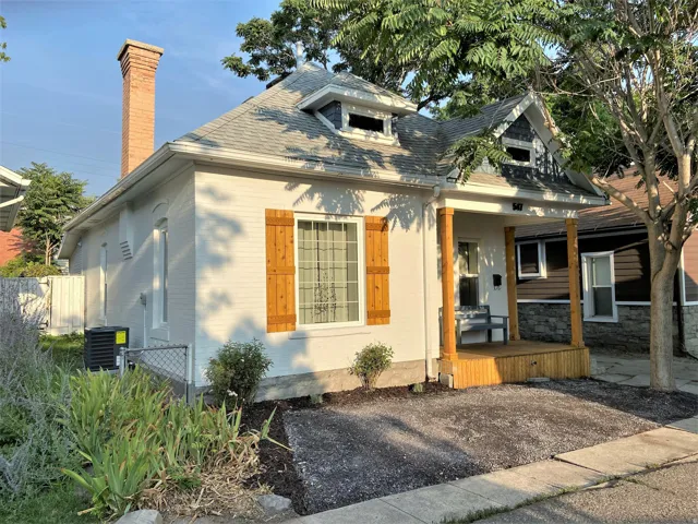 Bungalow-style home with a porch, brick siding, roof with shingles, and a chimney