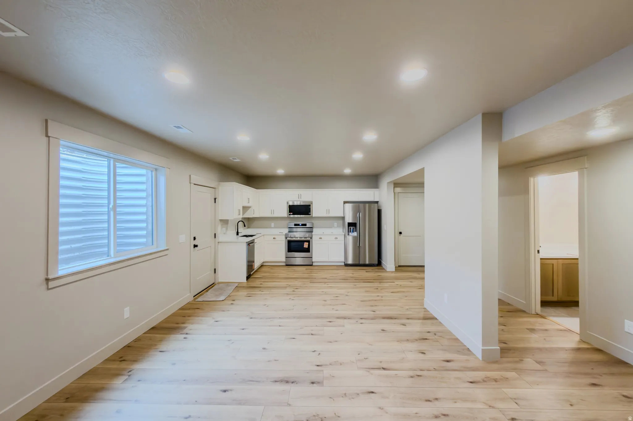 Kitchen featuring white cabinets, stainless steel appliances, light countertops, light wood-style floors, and recessed lighting