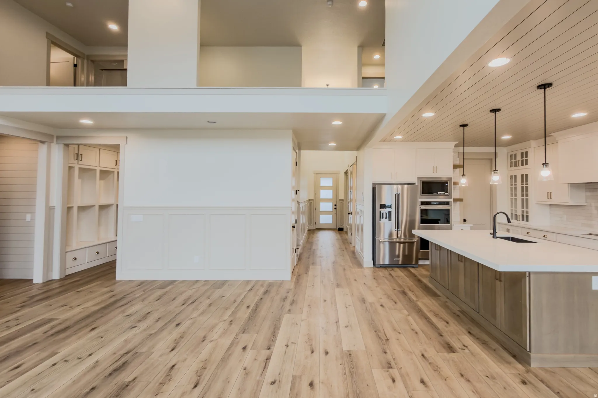 Kitchen with glass fronted cabinets, stainless steel appliances, dual tone cabinetry, a kitchen island with sink, and decorative light fixtures