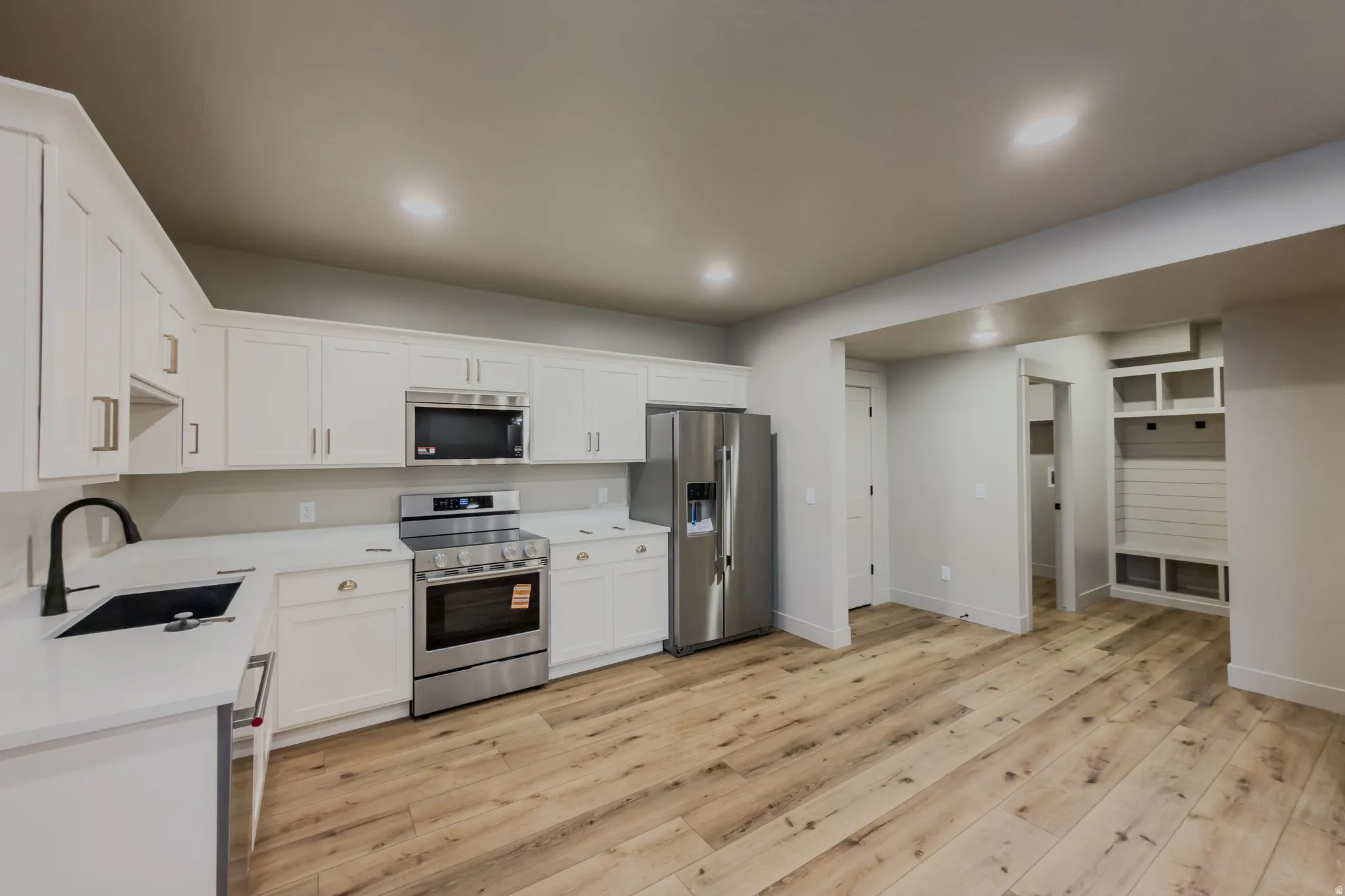 Kitchen with stainless steel appliances, white cabinetry, light wood-style flooring, recessed lighting, and light stone countertops