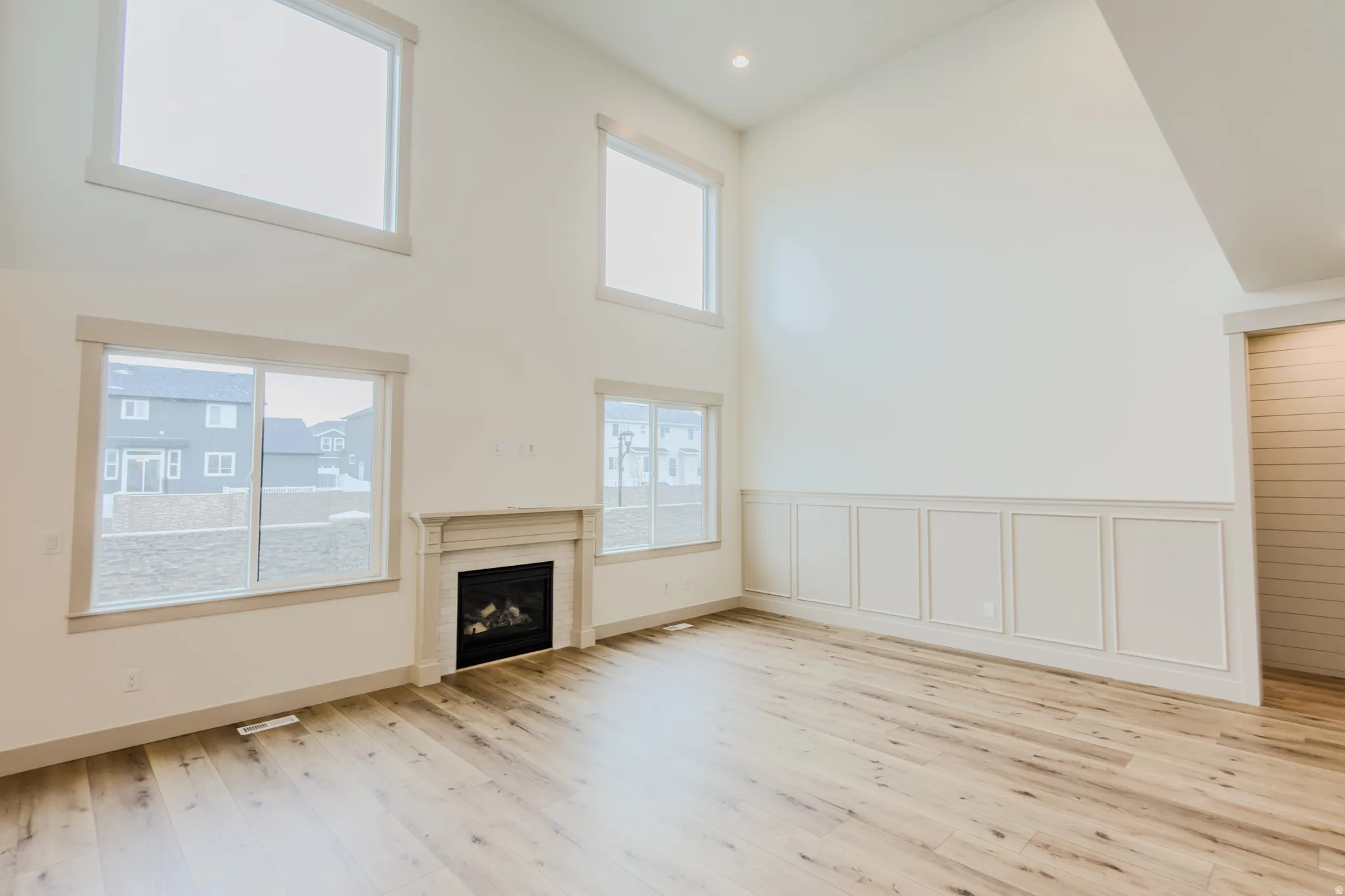 Unfurnished living room featuring a high ceiling, a fireplace, light wood-style flooring, recessed lighting, and a decorative wall