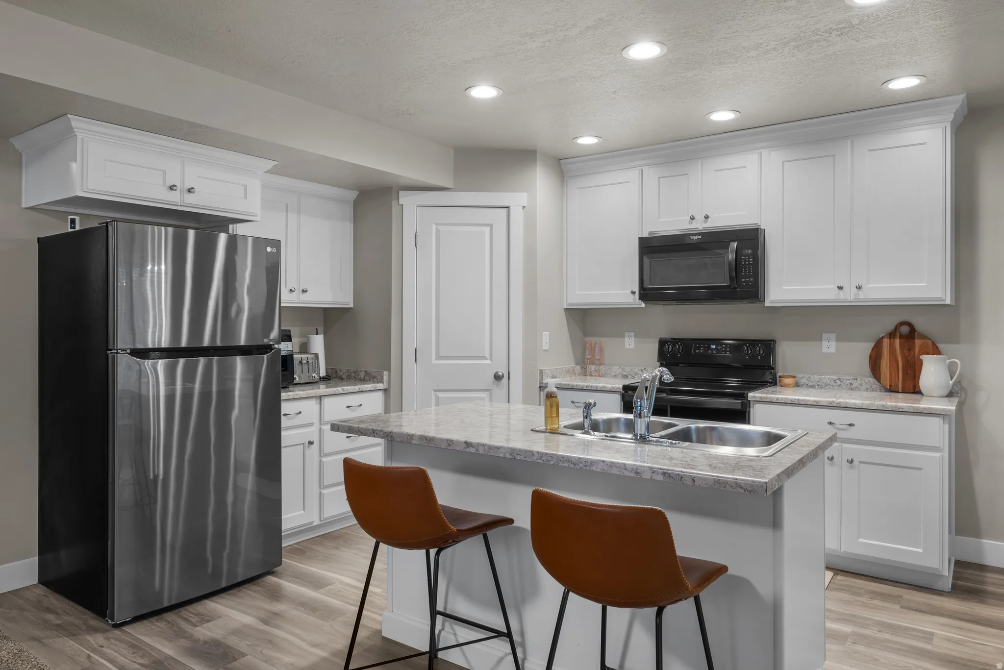 Kitchen featuring black appliances, white cabinets, light countertops, a kitchen island with sink, and light wood-type flooring