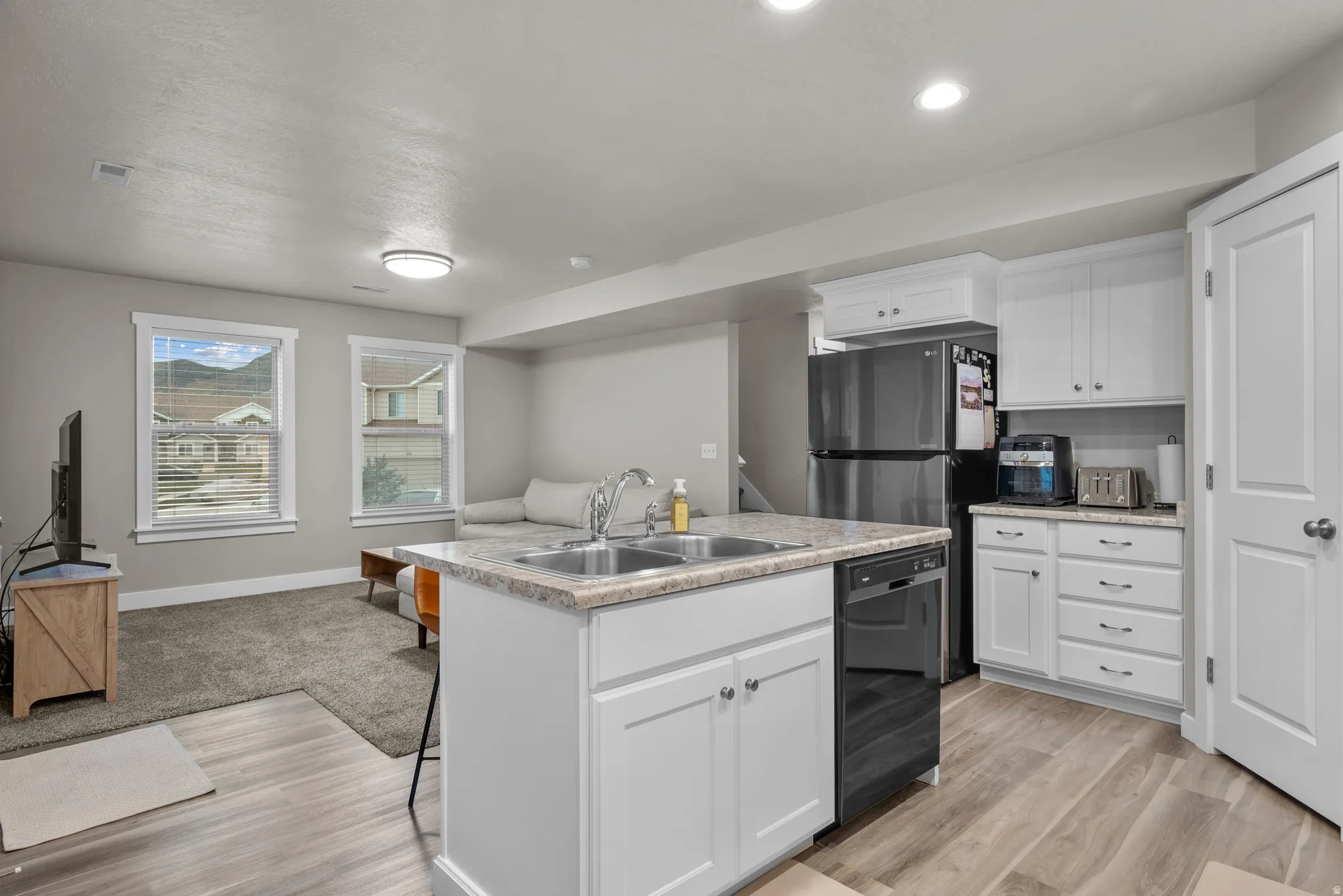 Kitchen featuring light countertops, white cabinetry, an island with sink, a breakfast bar area, and dishwasher