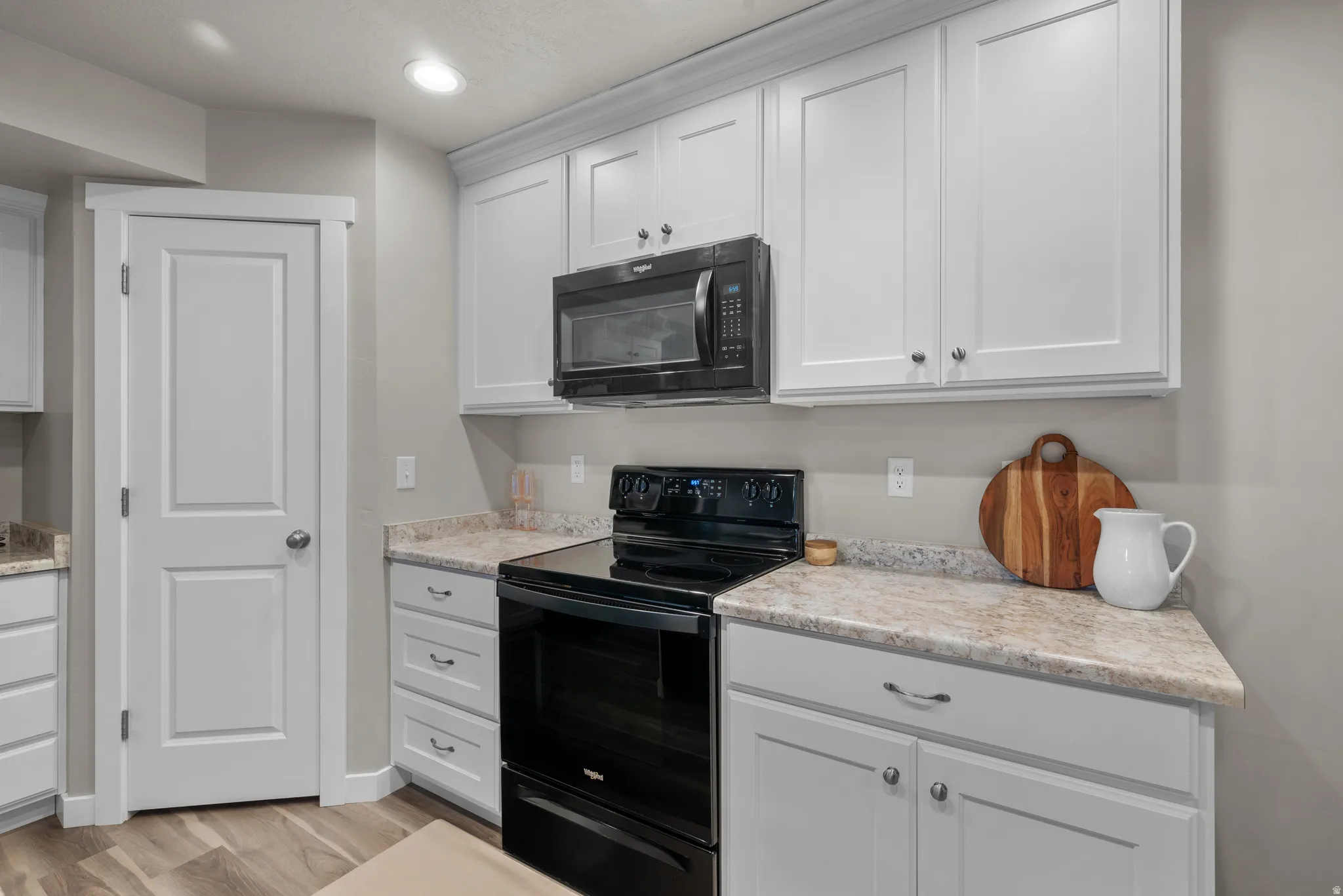 Kitchen featuring black appliances, white cabinetry, light wood finished floors, recessed lighting, and light stone counters