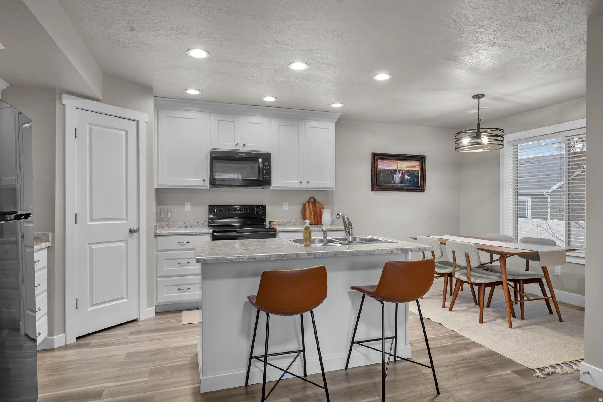 Kitchen featuring a center island with sink, black appliances, a textured ceiling, light wood-style flooring, and a kitchen breakfast bar