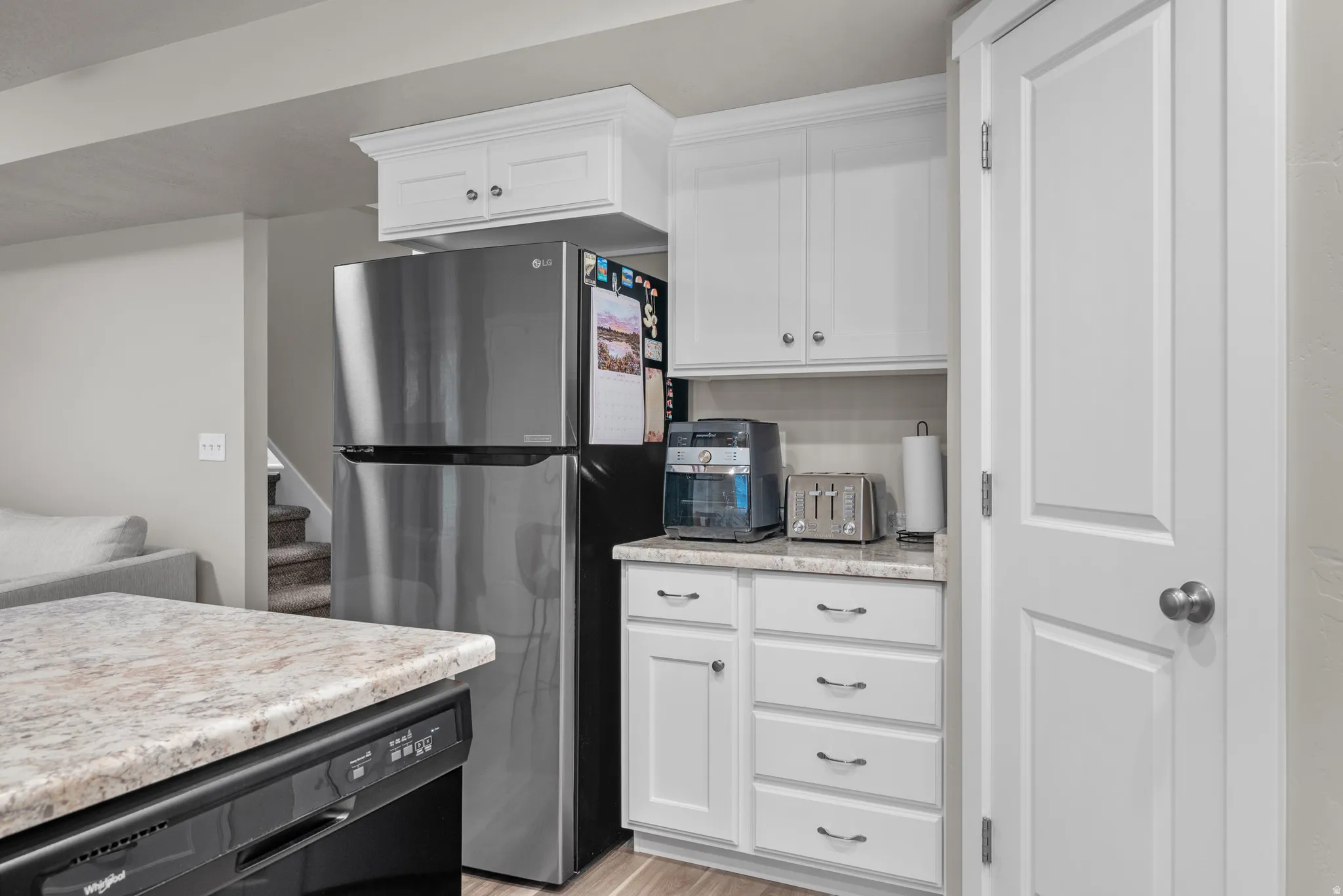 Kitchen featuring white cabinetry, freestanding refrigerator, dishwasher, and light wood-style floors