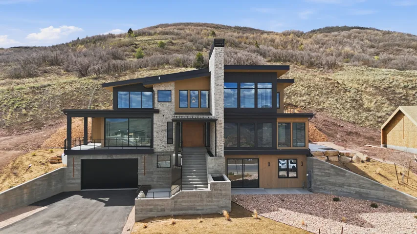 Modern home featuring a sunroom, asphalt driveway, an attached garage, a chimney, and a patio