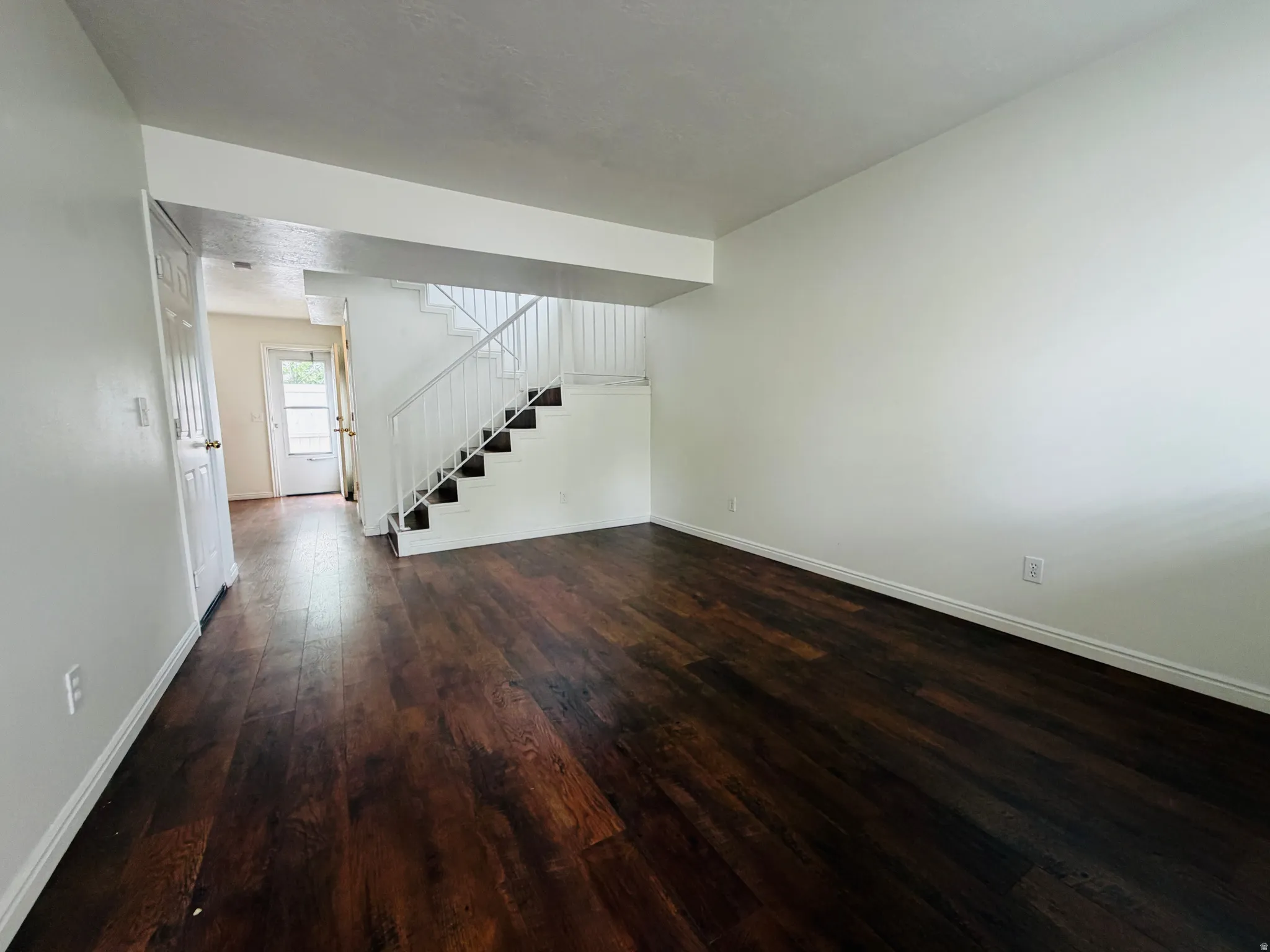 Unfurnished living room with stairs and dark wood-style flooring