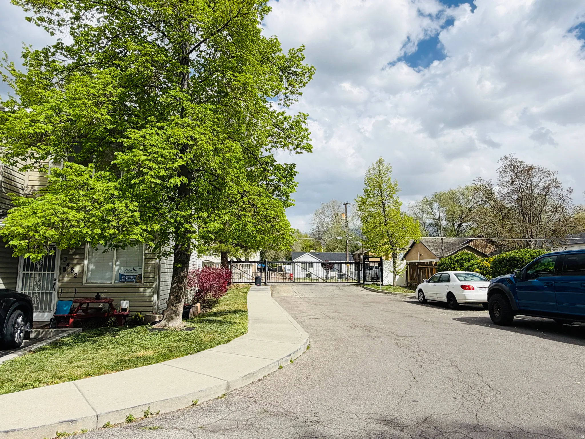 View of asphalt road featuring sidewalks, a residential view, a gate, and curbs