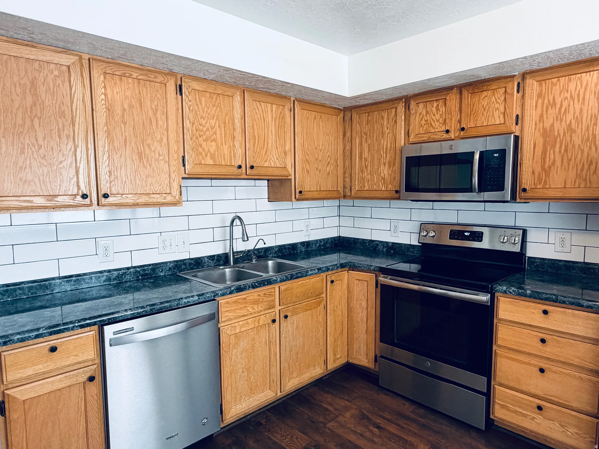 Kitchen featuring stainless steel appliances, tasteful backsplash, dark wood finished floors, wood finish cabinetry, and a textured ceiling