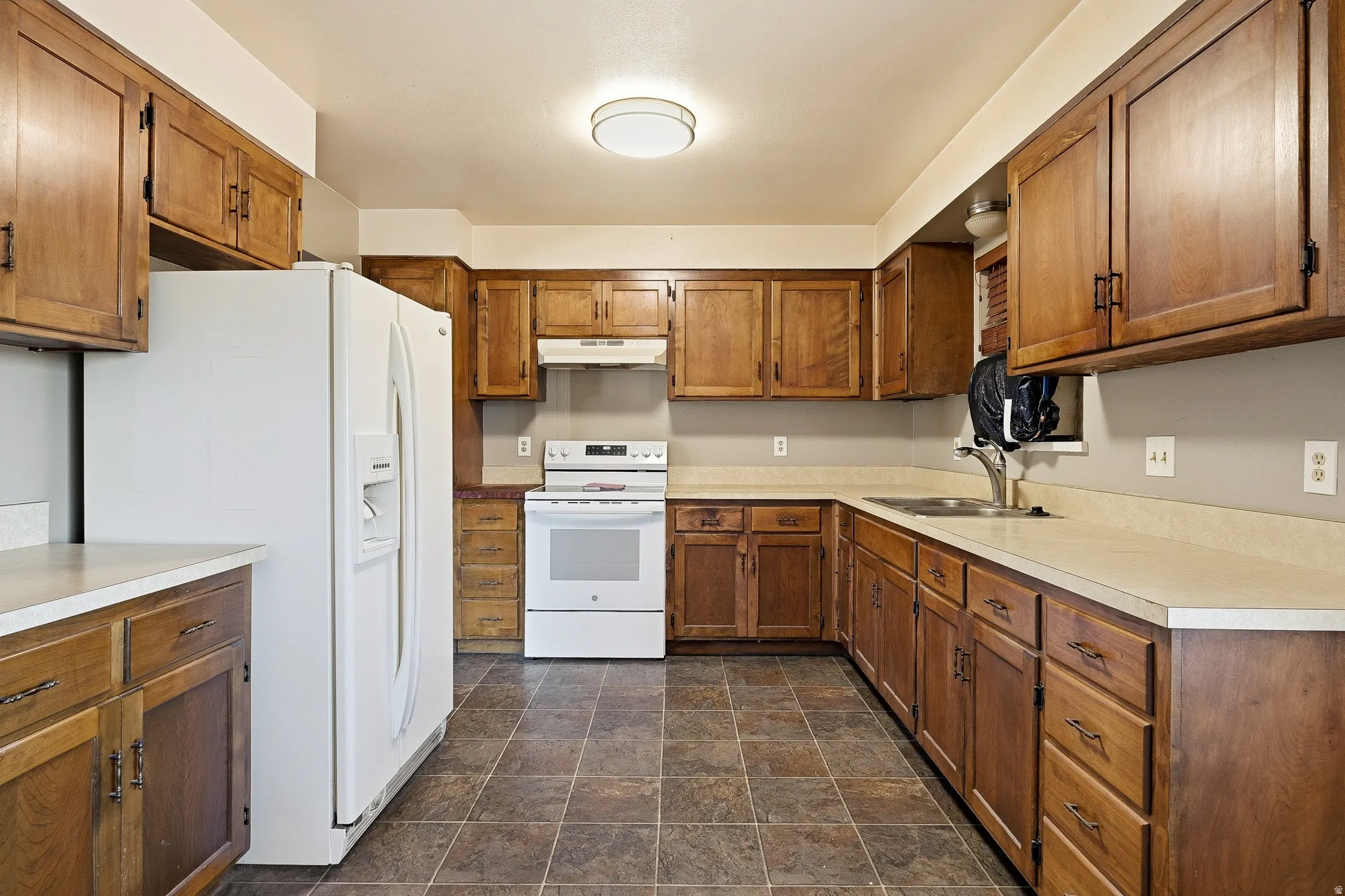 Kitchen featuring white appliances, wood finish cabinetry, stone finish flooring, and light countertops
