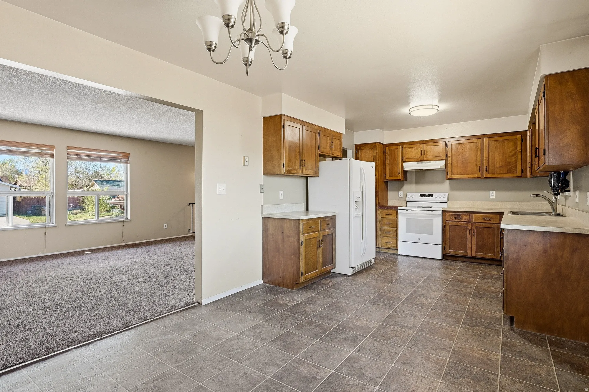 Kitchen with wood finish cabinets, white appliances, dark colored carpet, and light countertops