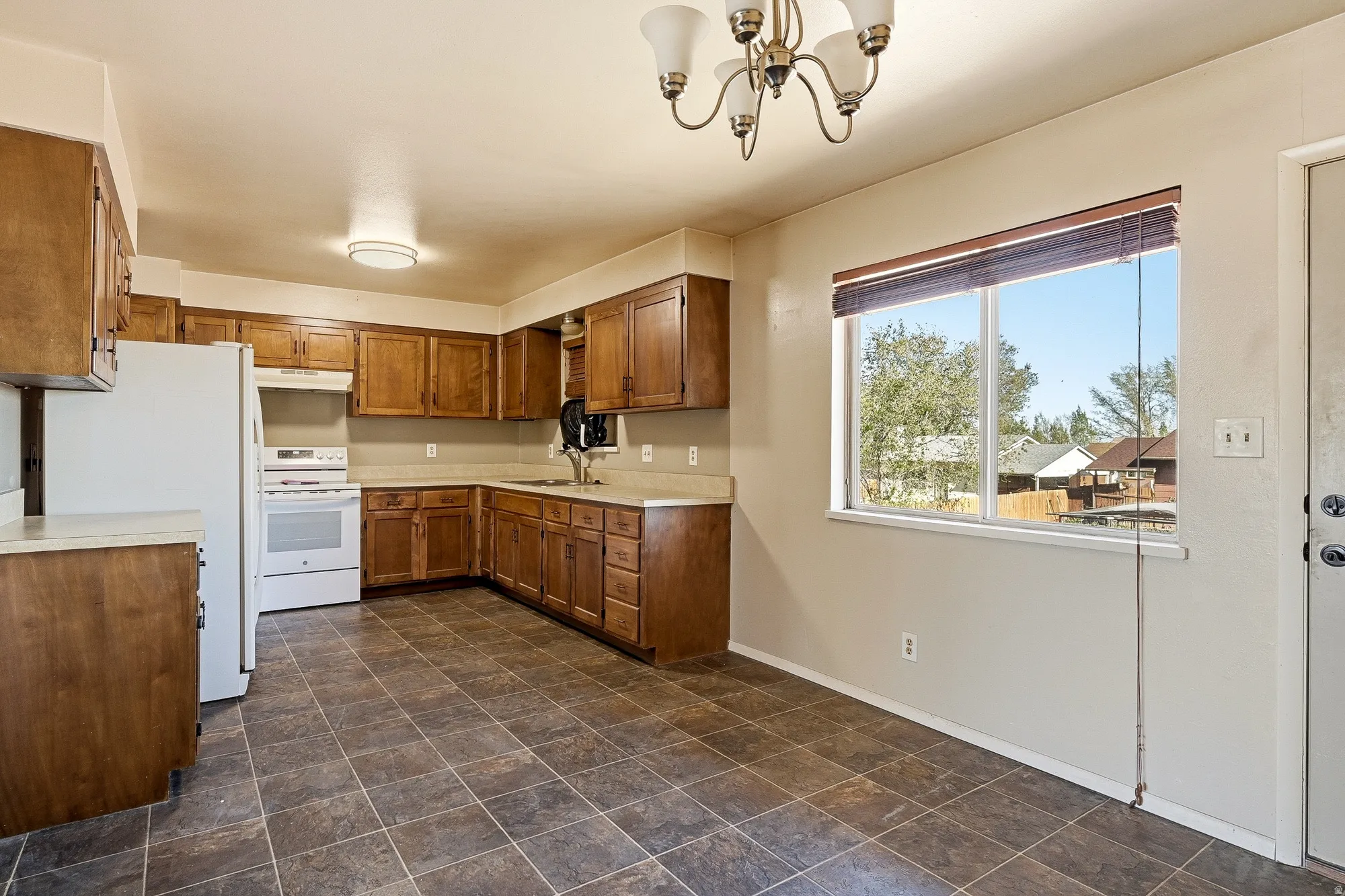 Kitchen featuring wood finish cabinets, white appliances, light countertops, hanging lights, and stone finish floors