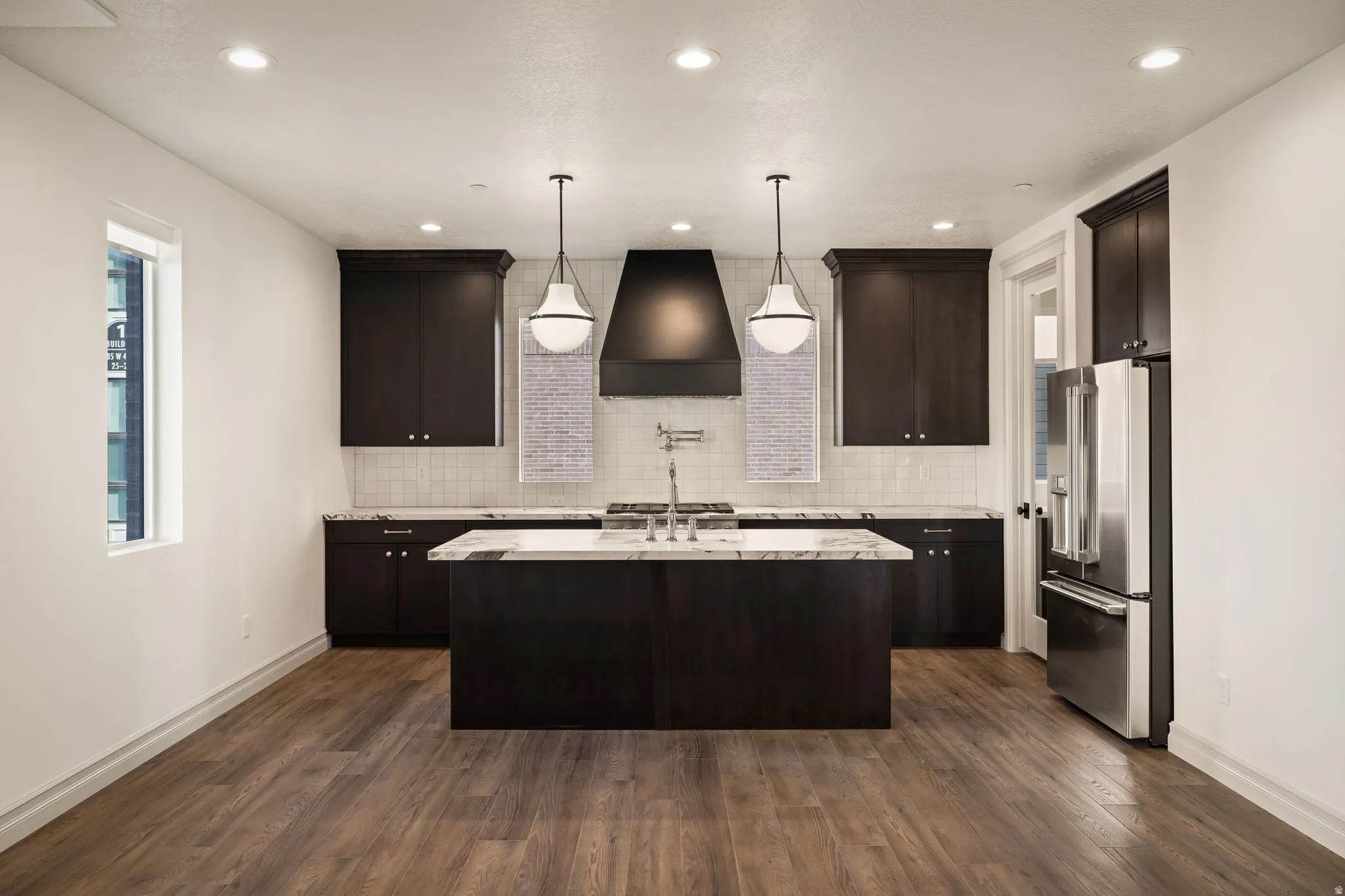 Photos of an exterior unit with the same finishes -Kitchen featuring dark wood finish cabinets, high quality fridge, a center island with sink, light stone countertops, and dark wood finished floors