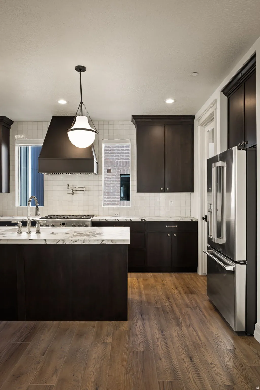 Photos of an exterior unit with the same finishes -Kitchen with high end refrigerator, dark wood finish cabinets, dark wood-style floors, light stone counters, and tasteful backsplash