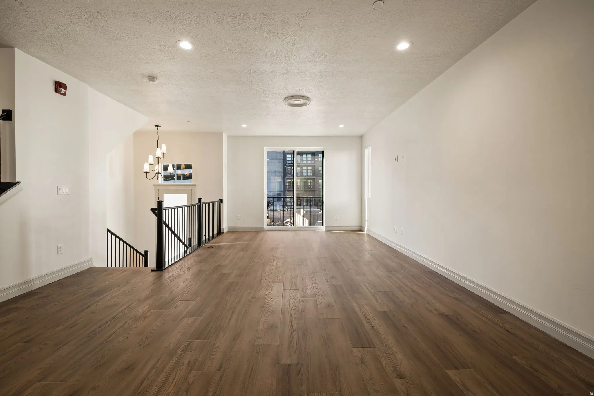 Photos of an exterior unit with the same finishes -Unfurnished living room featuring dark wood-style flooring, a textured ceiling, and a chandelier