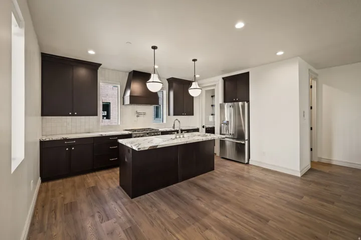 Photos of an exterior unit with the same finishes - Kitchen with dark wood finish cabinetry, stainless steel appliances, light stone counters, an island with sink, and dark wood finished floors