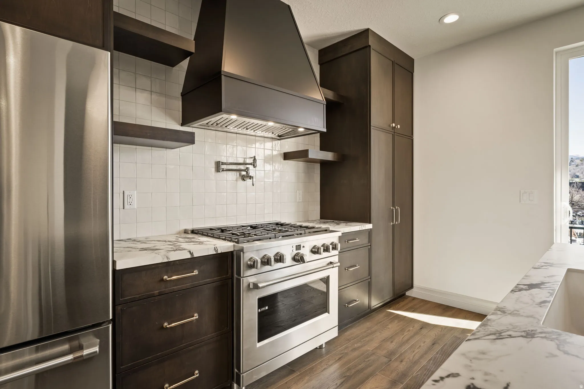 Kitchen with stainless steel appliances, dark wood finish cabinetry, dark wood-style floors, light stone countertops, and recessed lighting