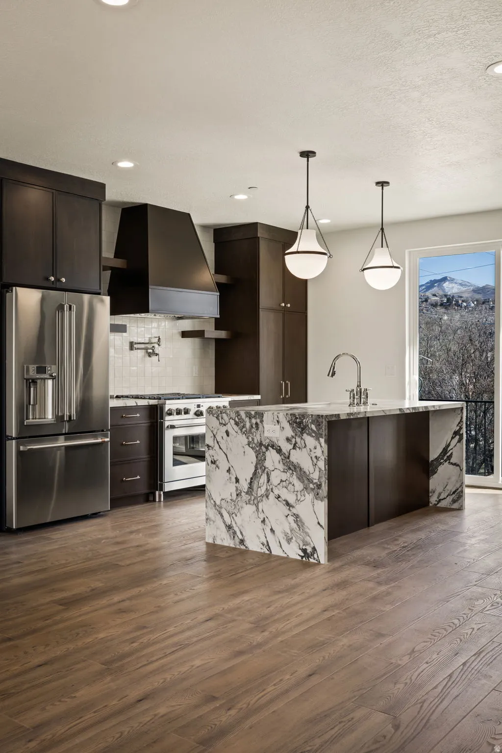 Kitchen featuring dark wood finish cabinets, high quality appliances, light stone counters, a kitchen island with sink, and dark wood finished floors