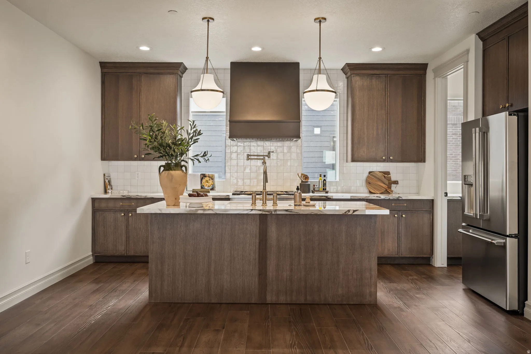 Kitchen featuring high quality fridge, light stone counters, a kitchen island with sink, and dark wood finish cabinetry