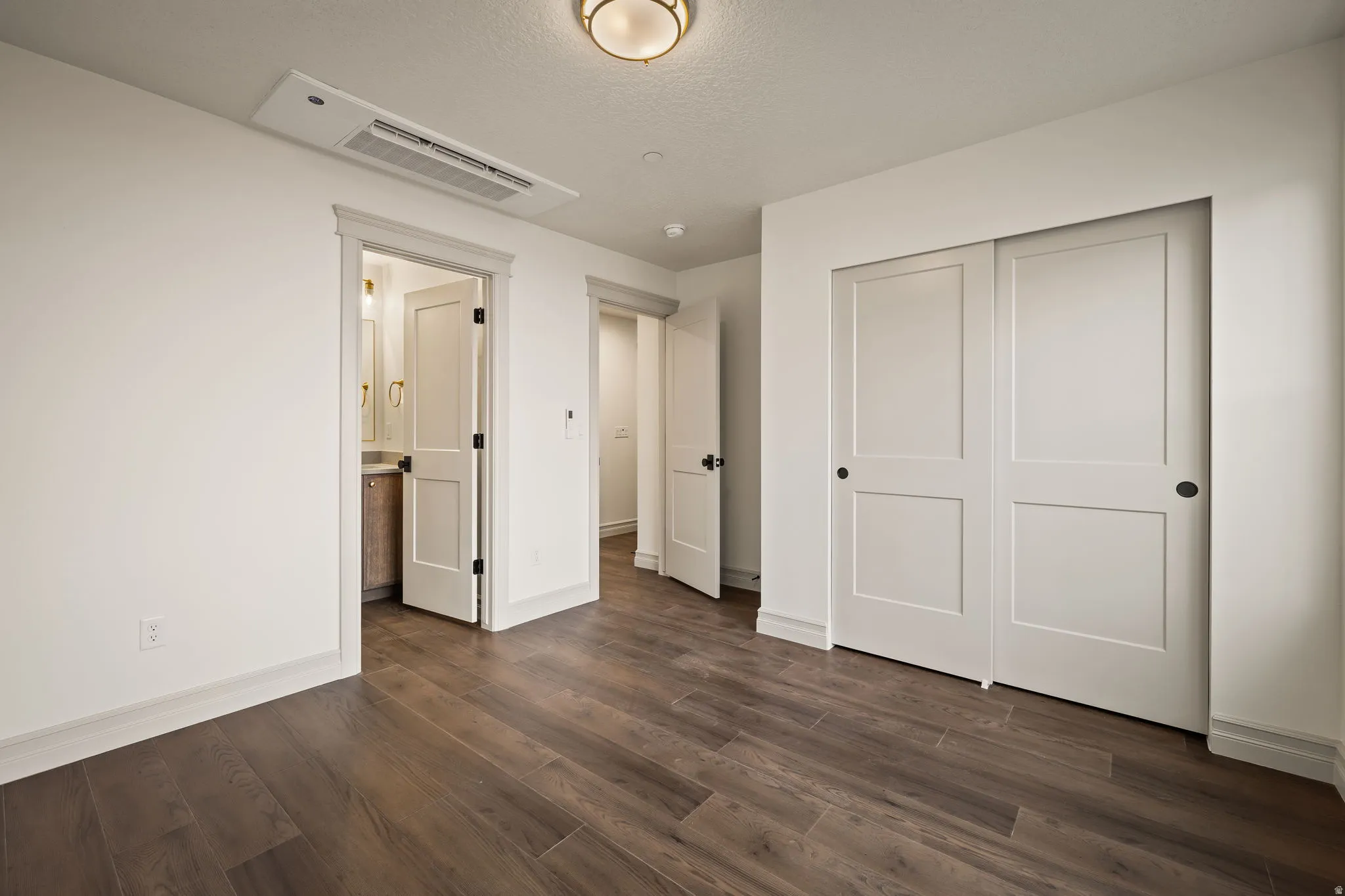 Unfurnished bedroom with dark wood-style floors, a closet, ensuite bathroom, and a textured ceiling