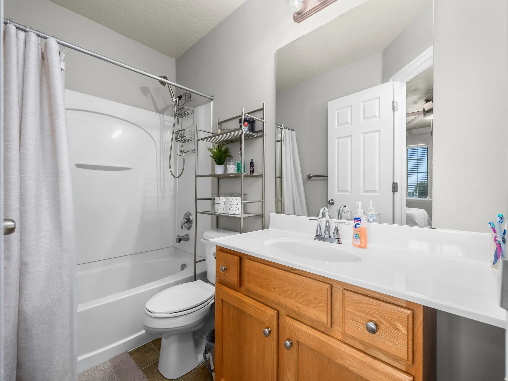 Ensuite bathroom featuring vanity, shower / bath combo, dark tile patterned flooring, and ceiling fan