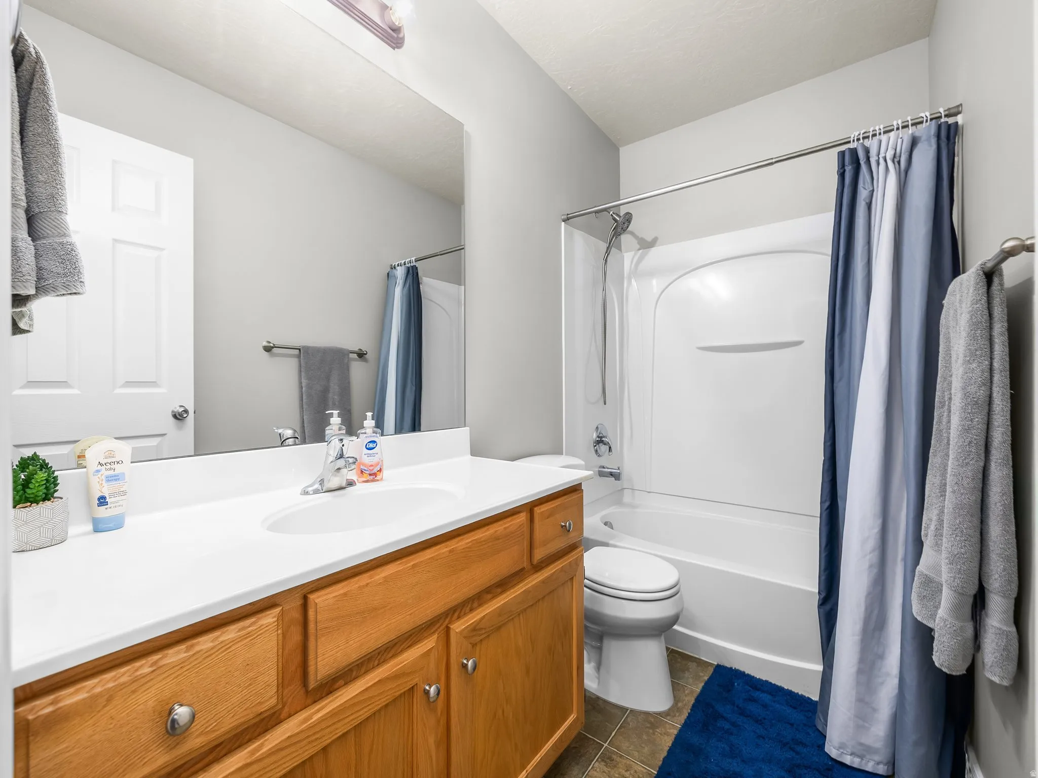 Full bath with vanity, shower / tub combo with curtain, and dark tile patterned flooring
