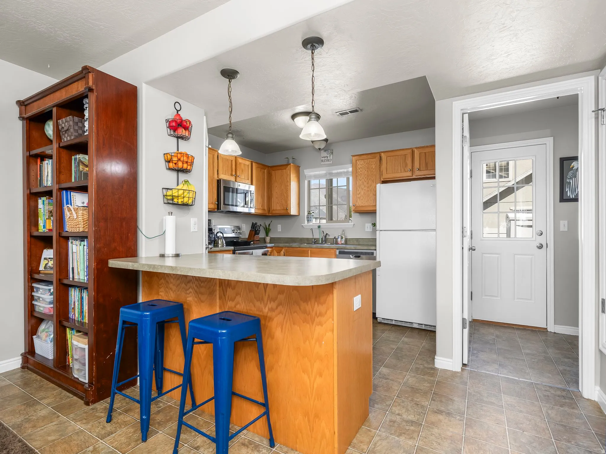 Kitchen with stainless steel appliances, wood finish cabinetry, a kitchen bar, a peninsula, and pendant lighting